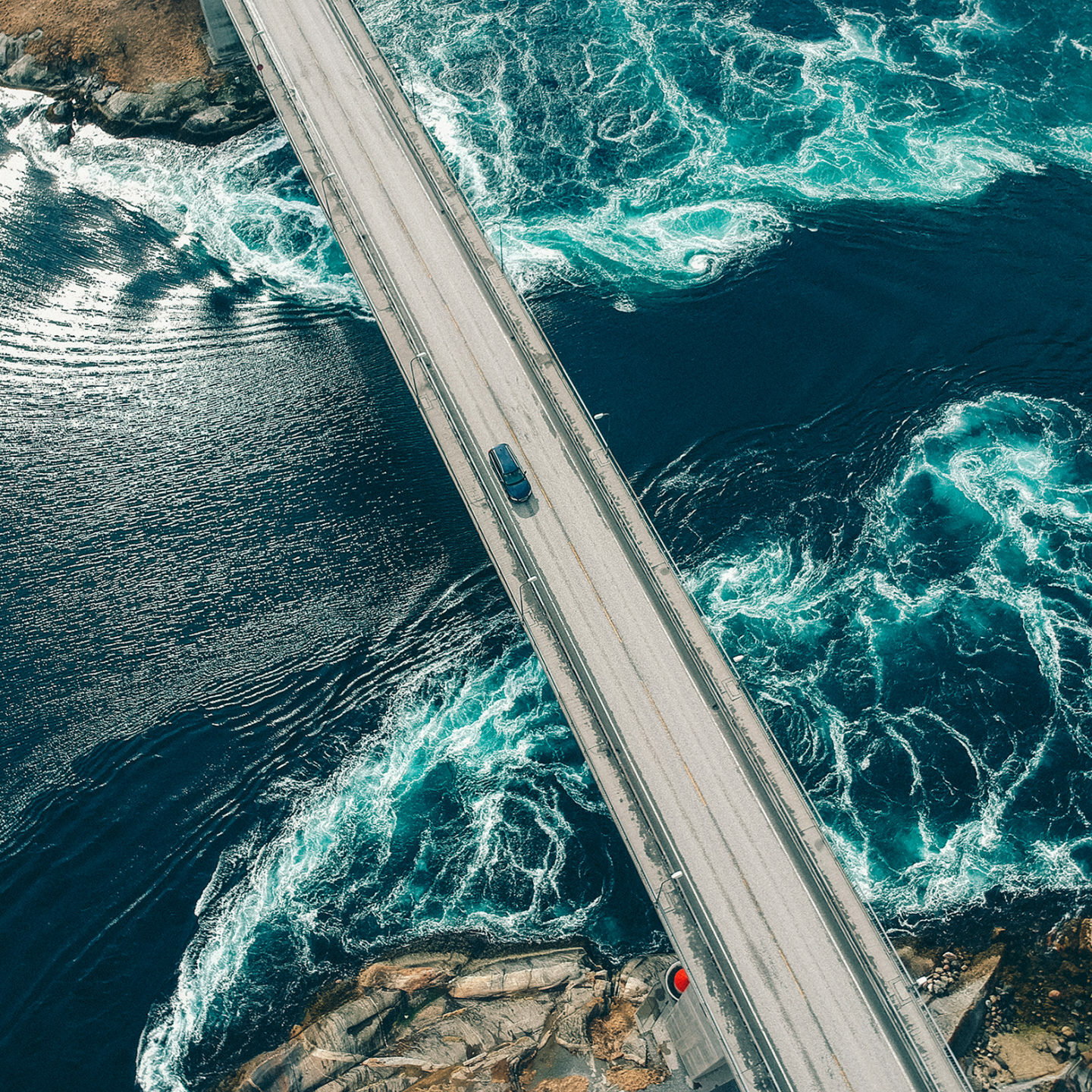 Torrents creating patterns in turquoise water underneath a bridge with a car traveling across it at Salstraumen near Bodo Norway